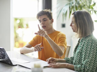 Waist-up view of high school student’s online education with parent assistance. Part of lifestyle series depicting deaf family and friends.