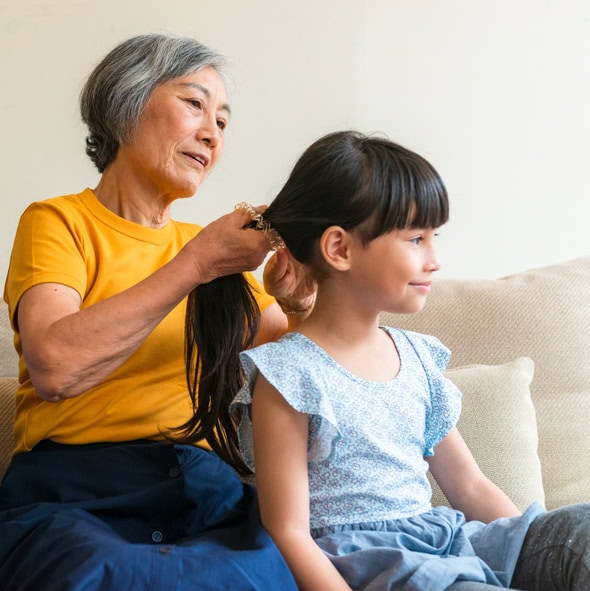 A young girl smiles as her grandmother carefully fixes her ponytail.